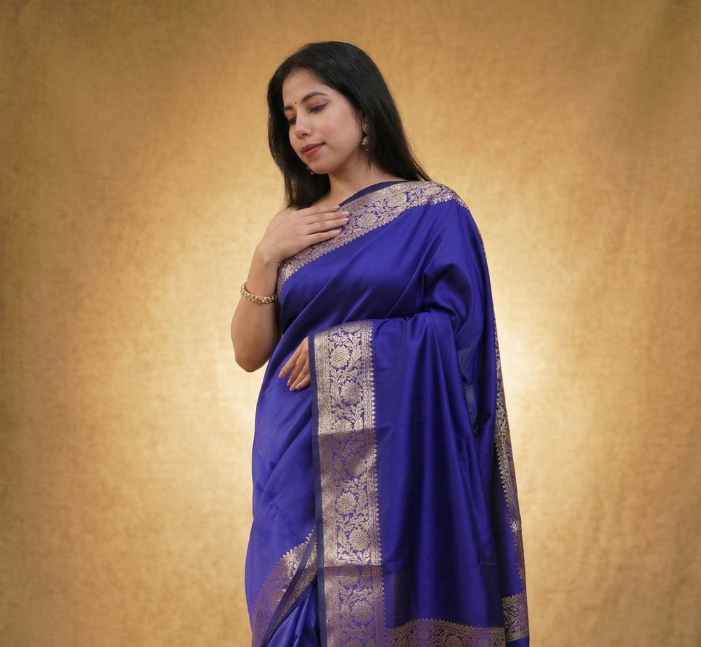 Woman wearing a blue saree with a gold border against a beige background